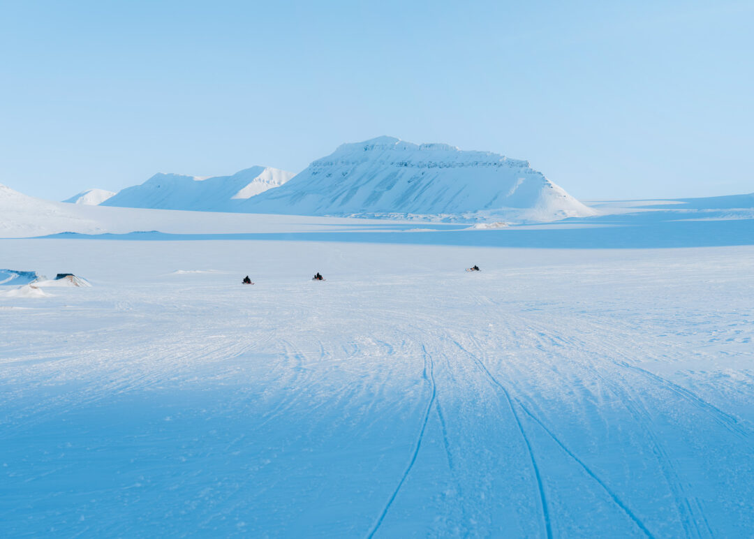 Snowmobile track across Arctic snow toward Svalbard mountains under a clear blue sky