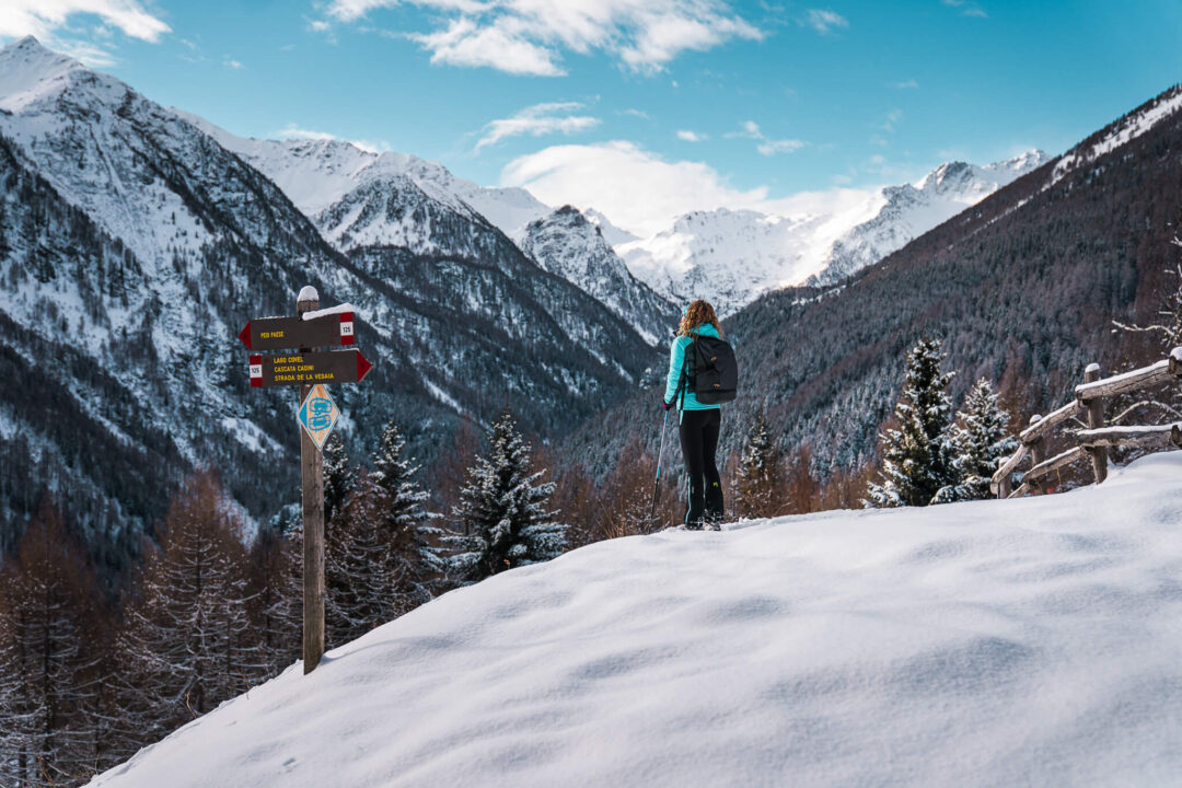 Snowshoer stands on snowy path in the Dolomites mountain valley beside trail signs, alpine winter landscape