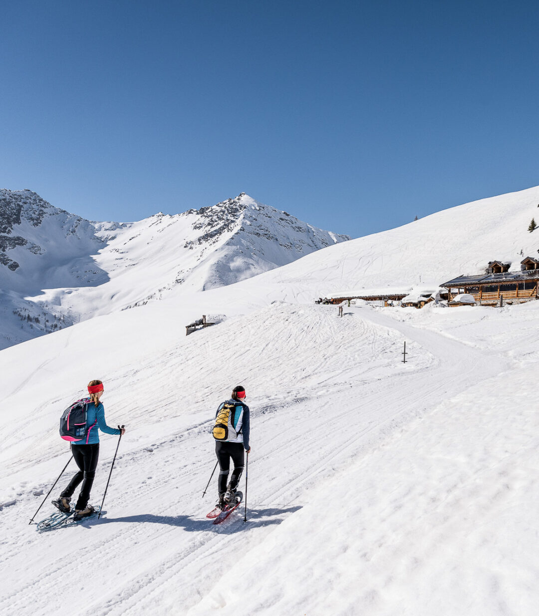 Guided snowshoeing in the snowy Dolomites with two hikers on a mountain trail past alpine huts