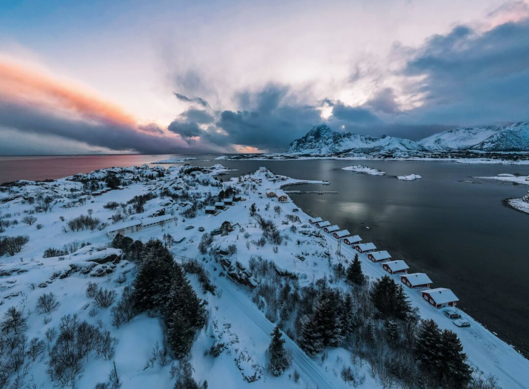 Snowy Lofoten fjord at dusk with scattered cabins, snowy fields and mountains under a cloudy sky