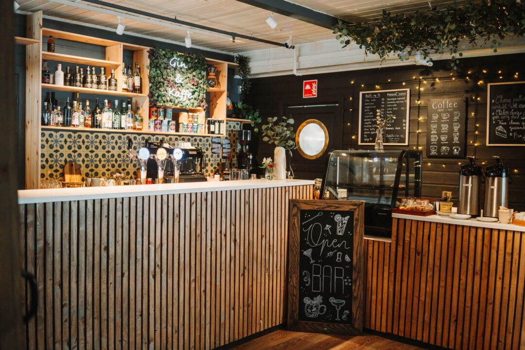 Cafe bar counter with coffee menu chalkboards and shelves of drinks inside a warm timber interior