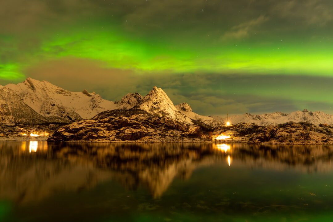 Northern lights (aurora borealis) over snowy mountains and calm fjord reflections in Lofoten at night