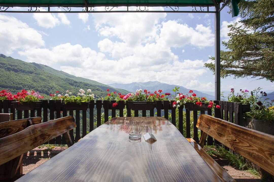 Wooden terrace table with colourful flowers overlooking green mountain valley scenery