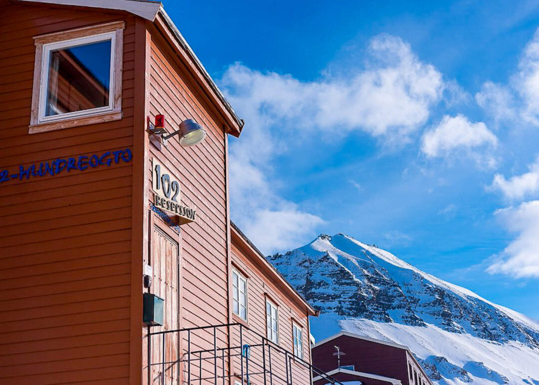 Lodge building with room number 102 against snowy Svalbard mountains and blue sky