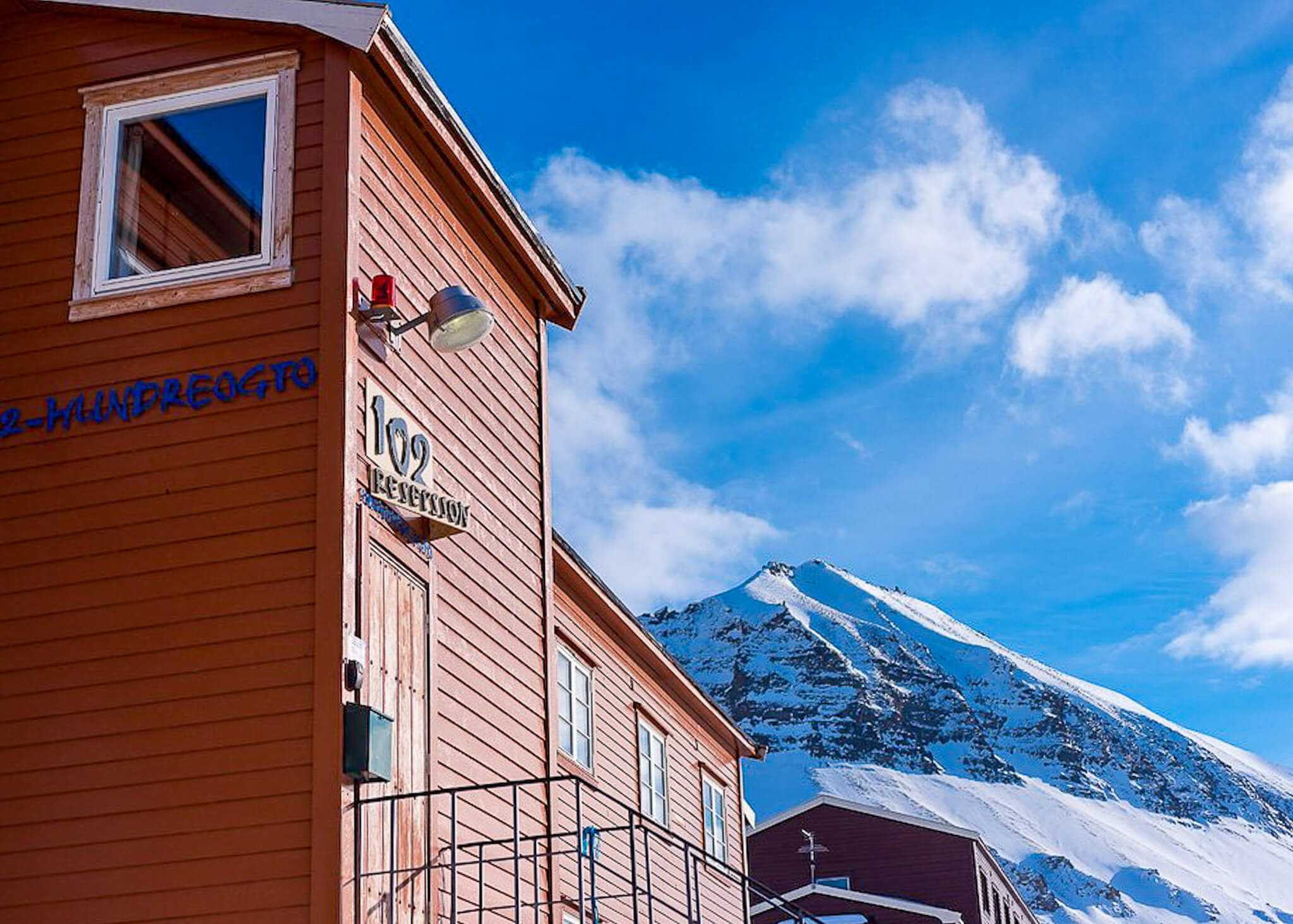 Lodge building with room number 102 against snowy Svalbard mountains and blue sky