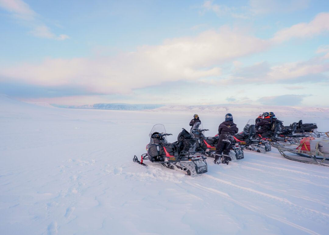 Snowmobilers on snowmobiles traverse the snowy Arctic plain in Svalbard at dusk