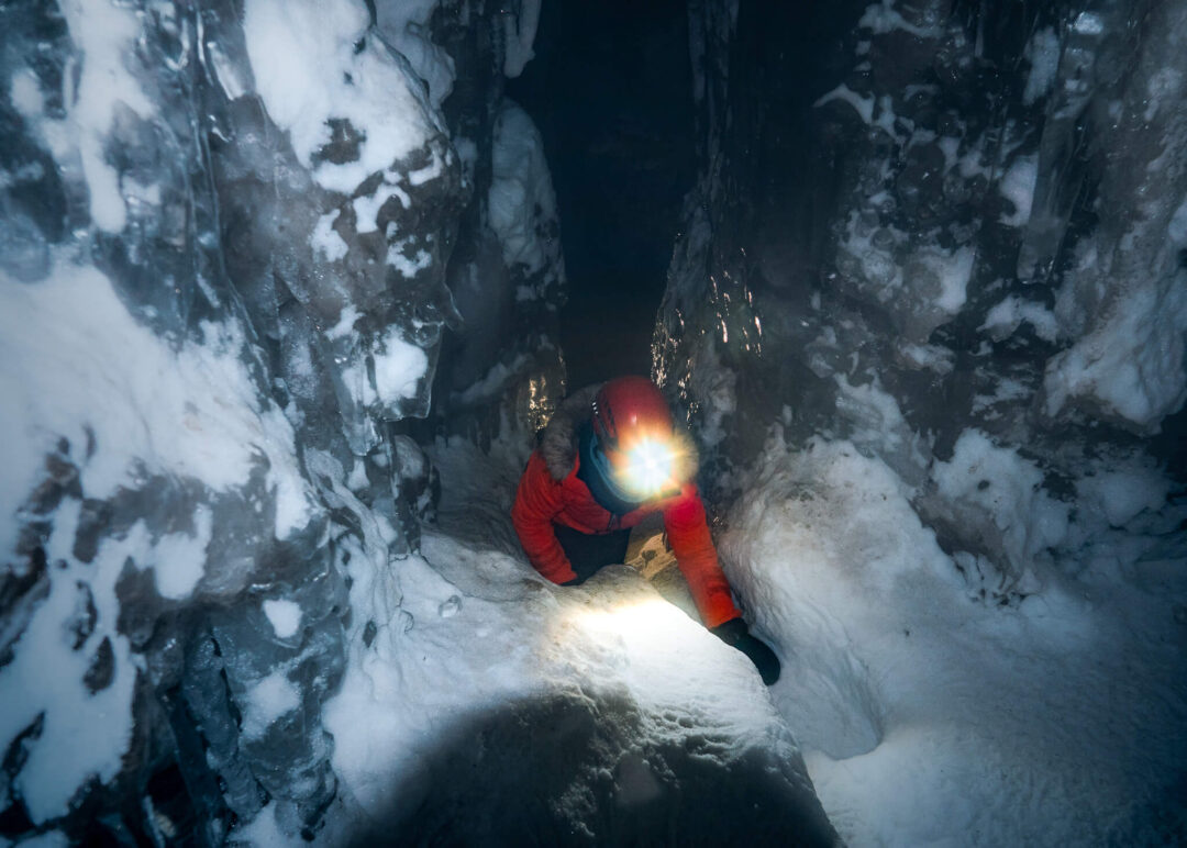Snowmobiler in a red suit rides through a snowy Svalbard canyon, headlight blazing at night