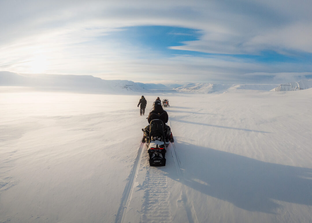 Snowmobiles ride across Svalbard snowfields under a dramatic Arctic sky