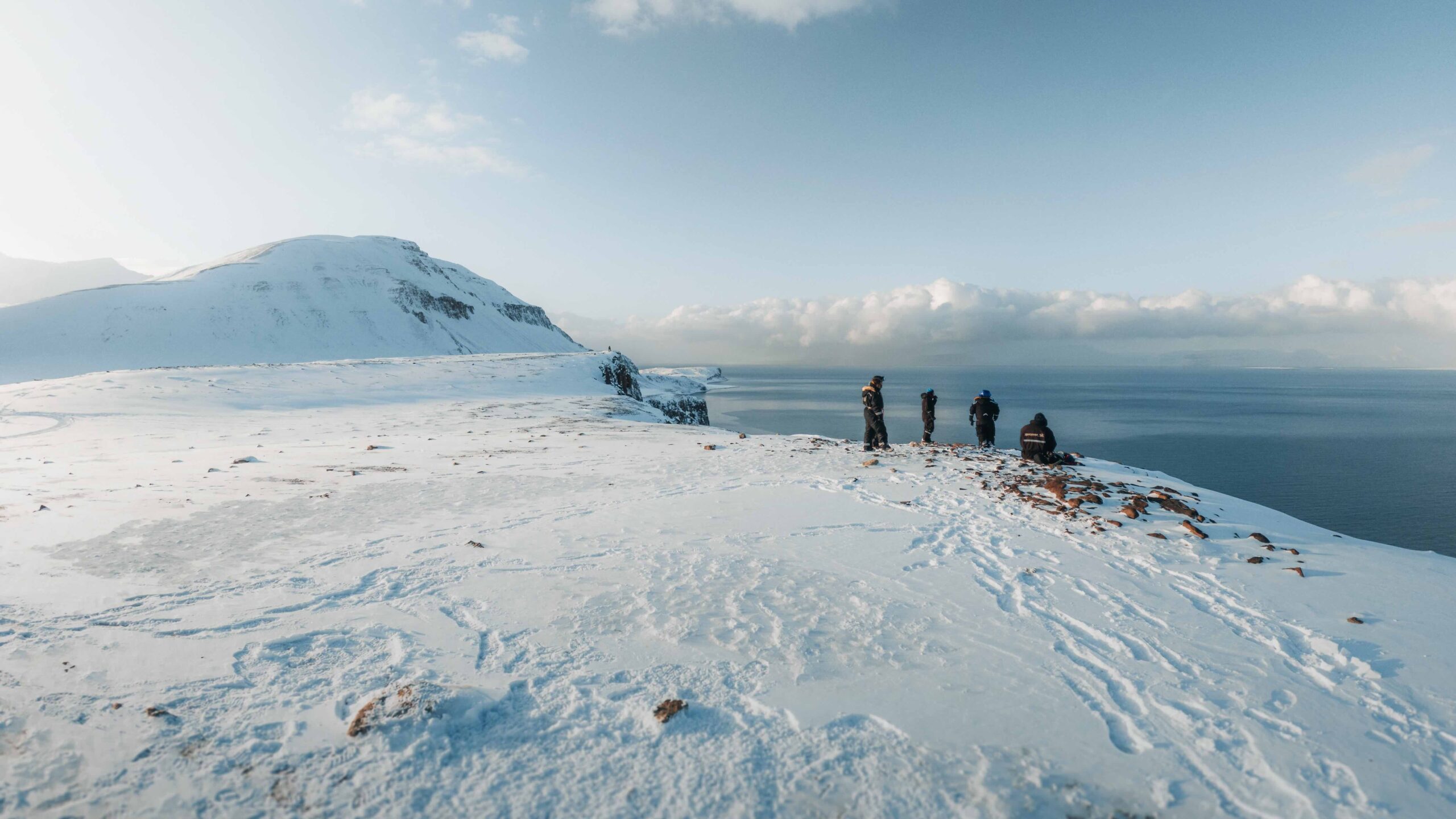 Snowmobile riders on a snowy Svalbard ridge overlooking Arctic mountains and the sea in the distance