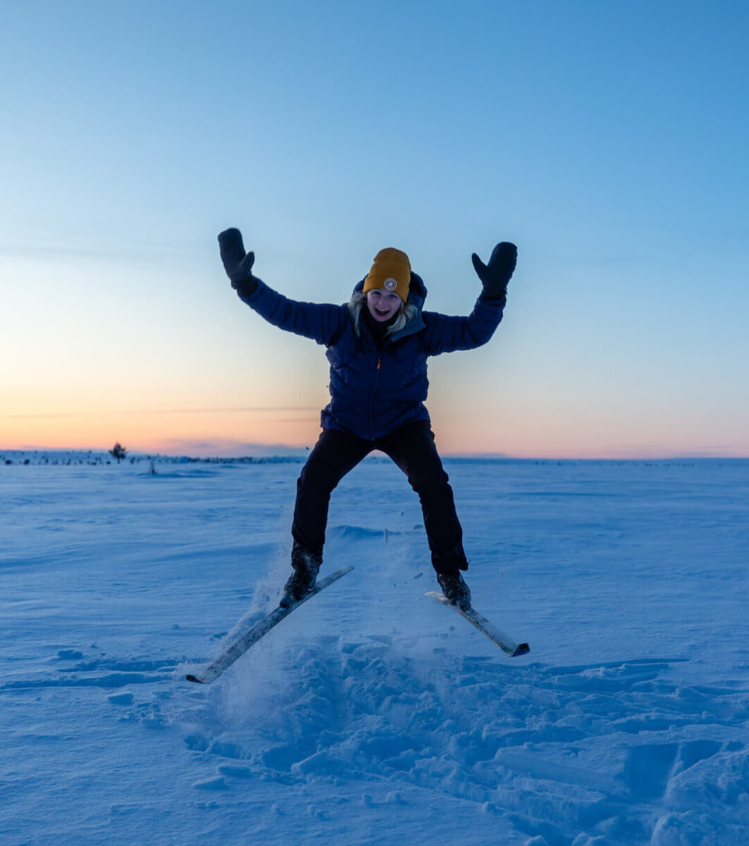 Backcountry skier joyfully jumping in snowy Lapland at dawn during a hut-to-hut ski expedition