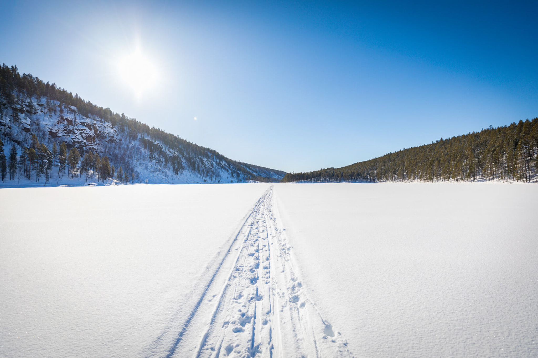 Ski track through snowy Lapland backcountry landscape with pine hills under bright winter sun