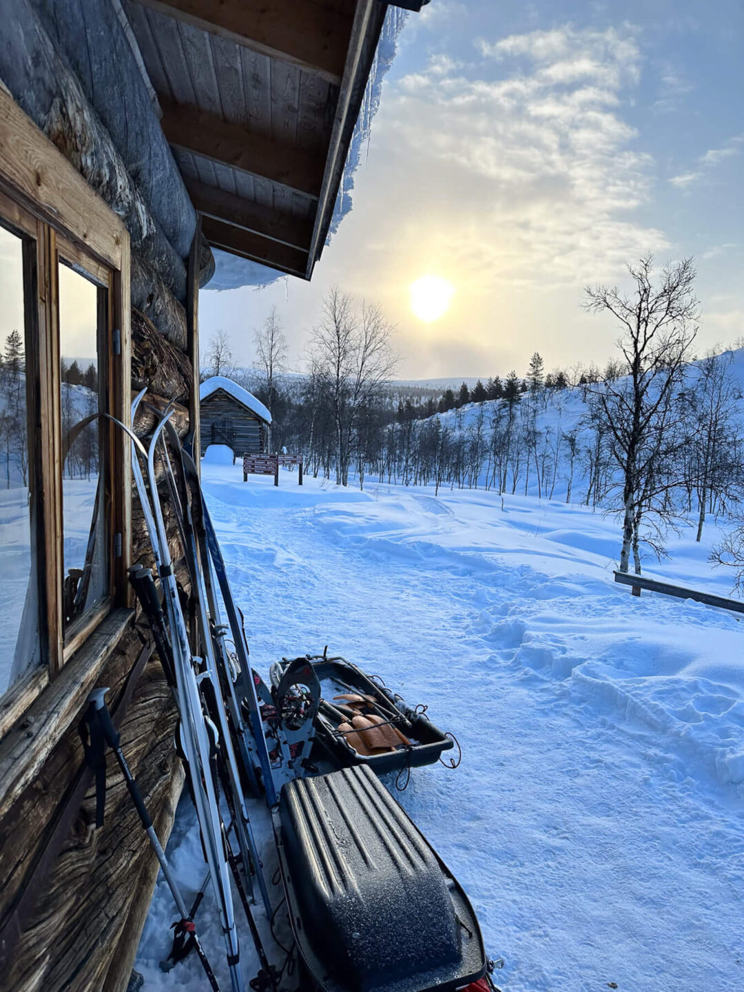 Ski gear outside a Lapland backcountry hut in snowy winter landscape at sunset, ready for hut-to-hut skiing