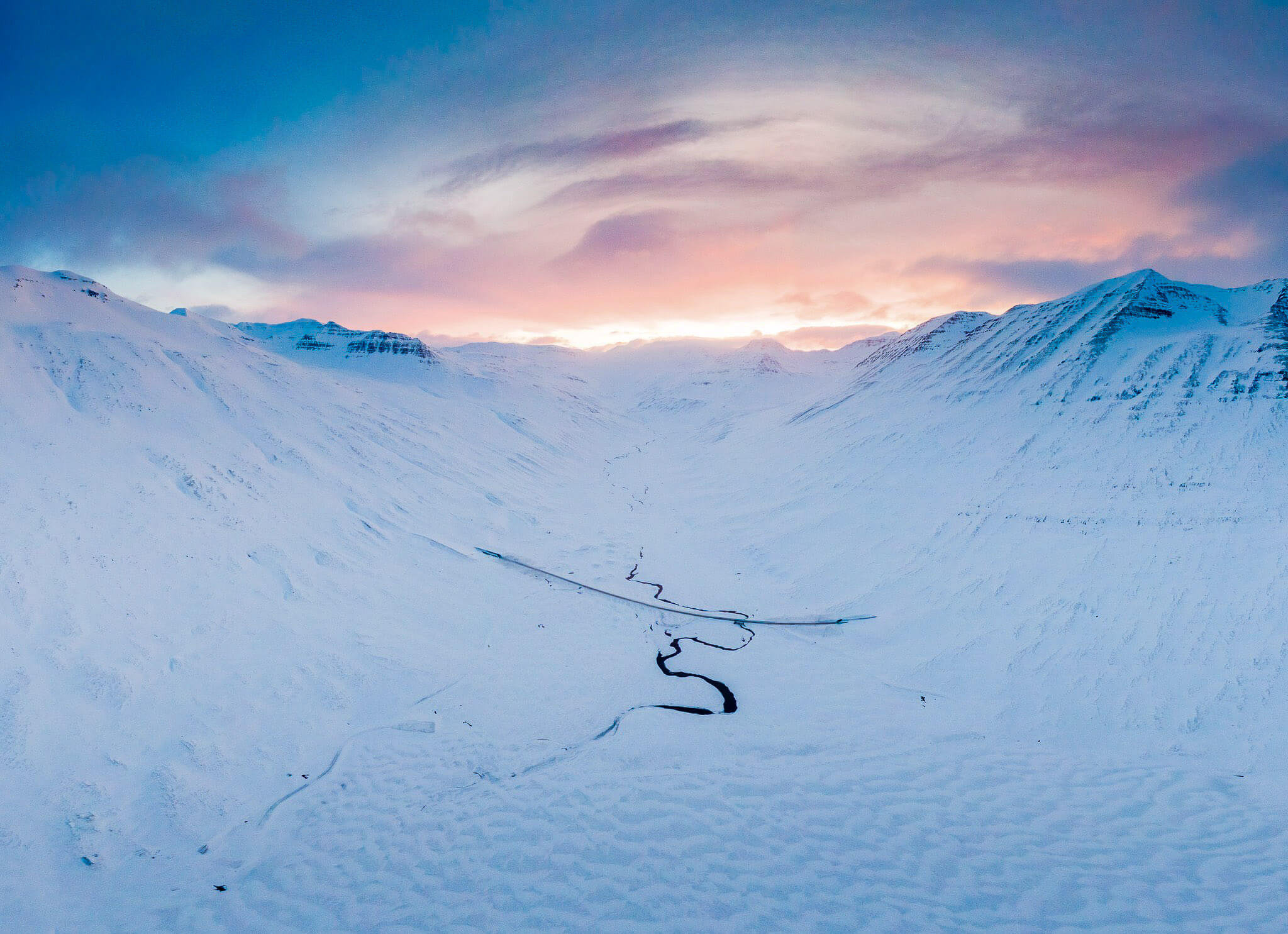 Snow-covered ski slope winding through Icelandic mountains at sunrise, winter multi-activity holiday landscape