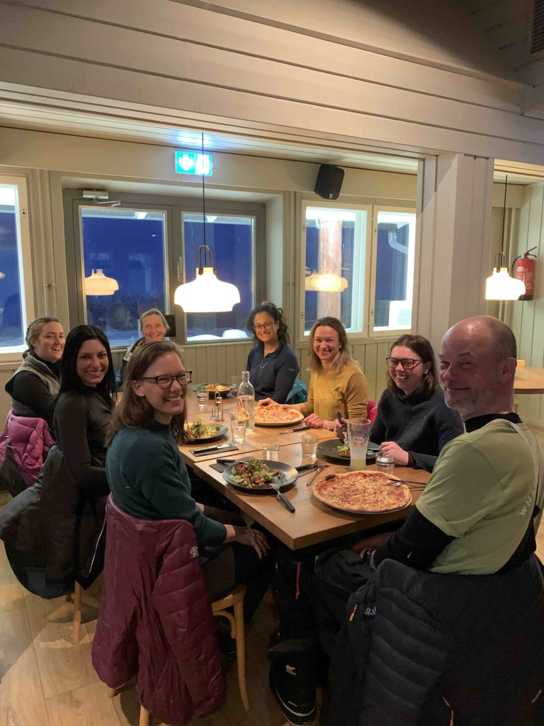 Women seated at a table eating pizza in an indoor ski hut dining room during a hut-to-hut expedition