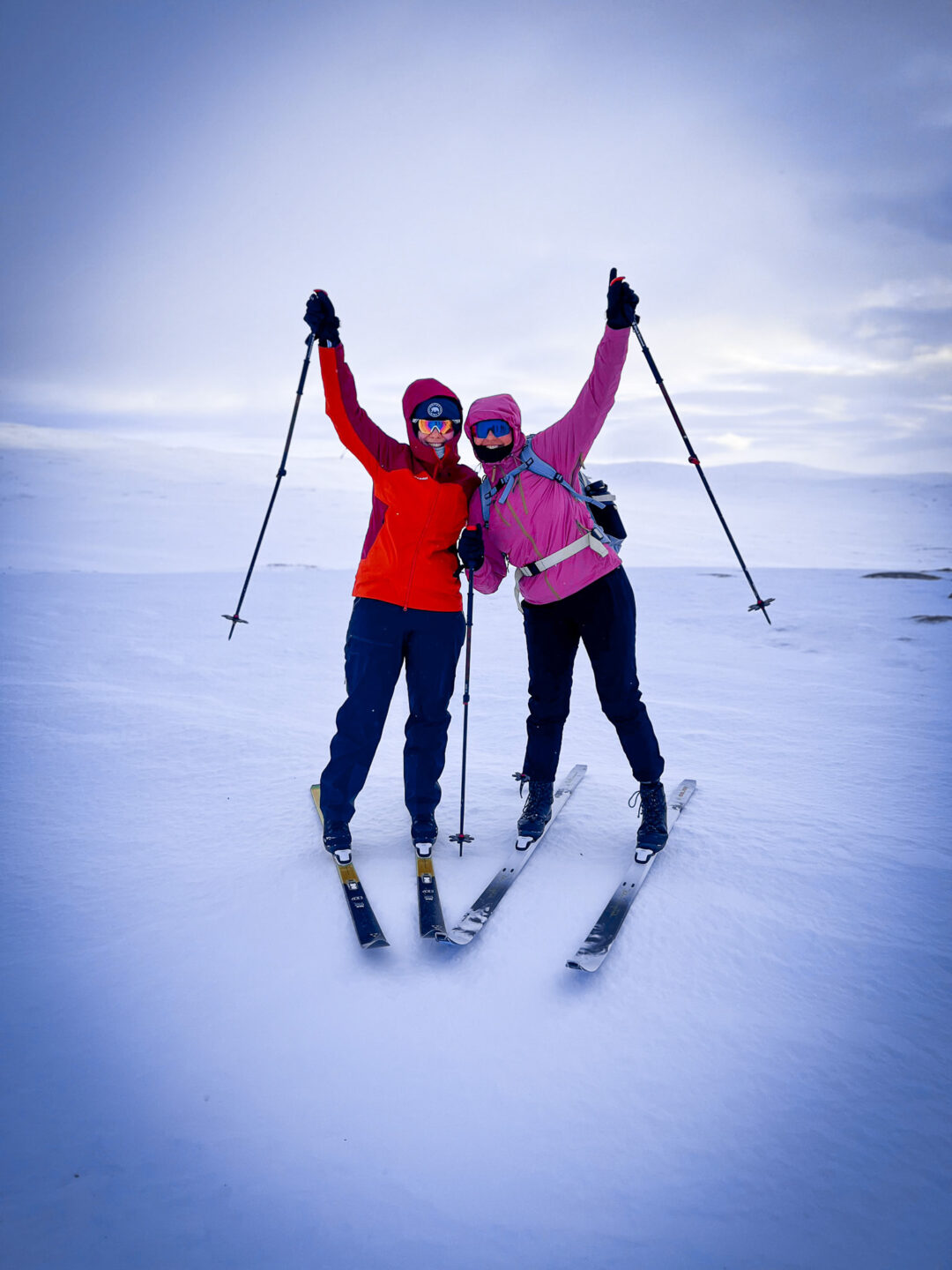 Two backcountry skiers in Lapland snow, arms up with trekking poles during a hut-to-hut skiing expedition
