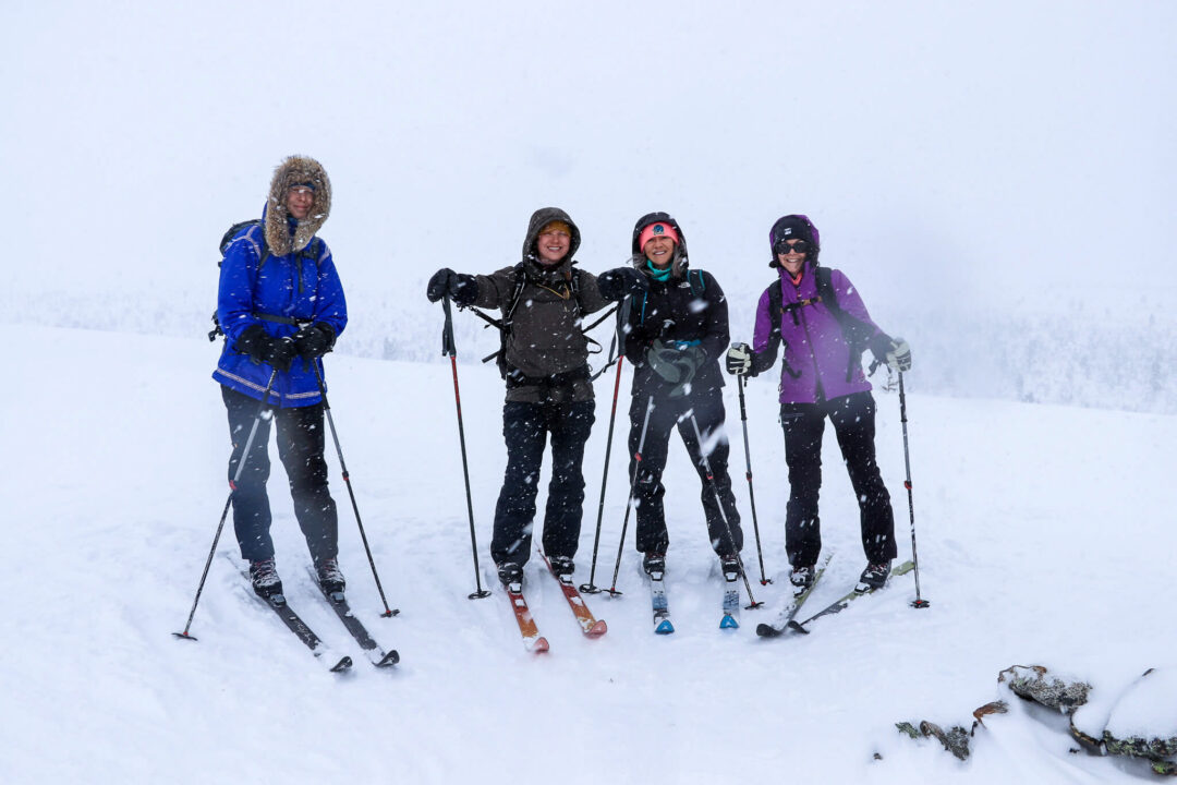 Backcountry skiers posing with skis and poles on a snowy Lapland hut-to-hut expedition in whiteout conditions
