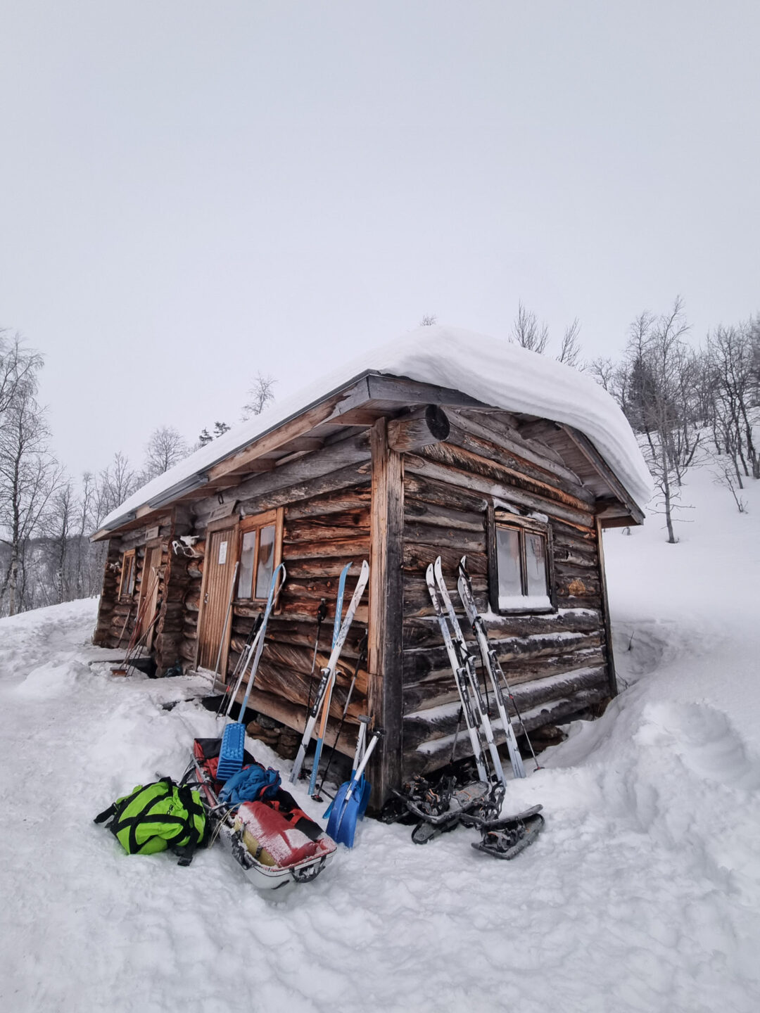 Snow-covered Arctic Circle ski hut with skis and snow gear outside in the winter wilderness