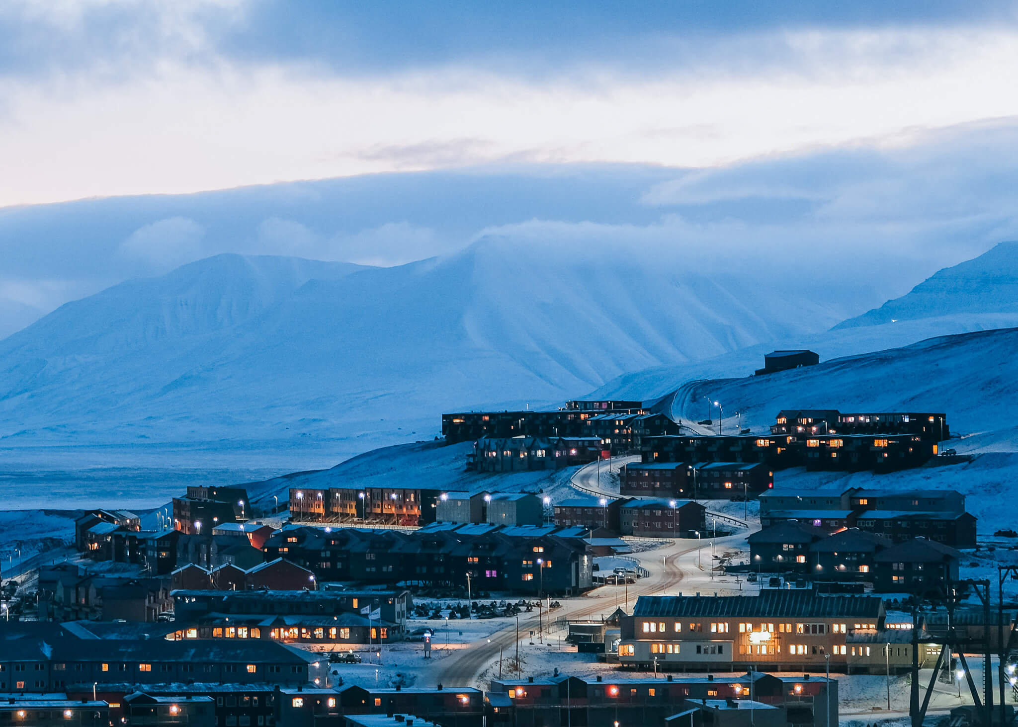 Twilight view of a snowy Svalbard settlement, with arctic buildings along the hillside
