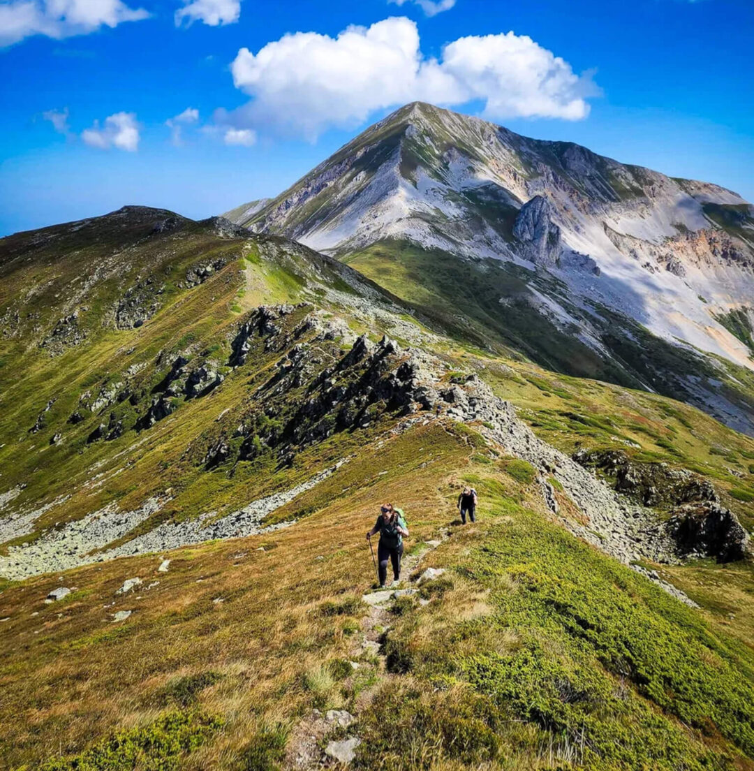 Women hiking along a mountain ridge with a volcanic peak in North Macedonia under blue sky