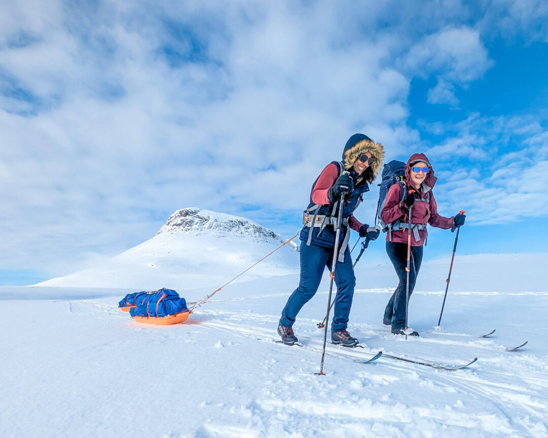 Two skiers trekking across snowy Arctic landscape with skis, poles and backpacks on a hut-to-hut expedition