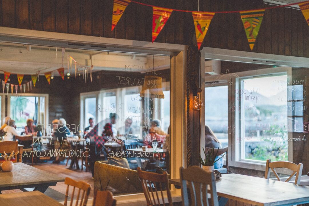 Rustic wooden café interior with tables, chairs, warm string lights and bunting flags by the window