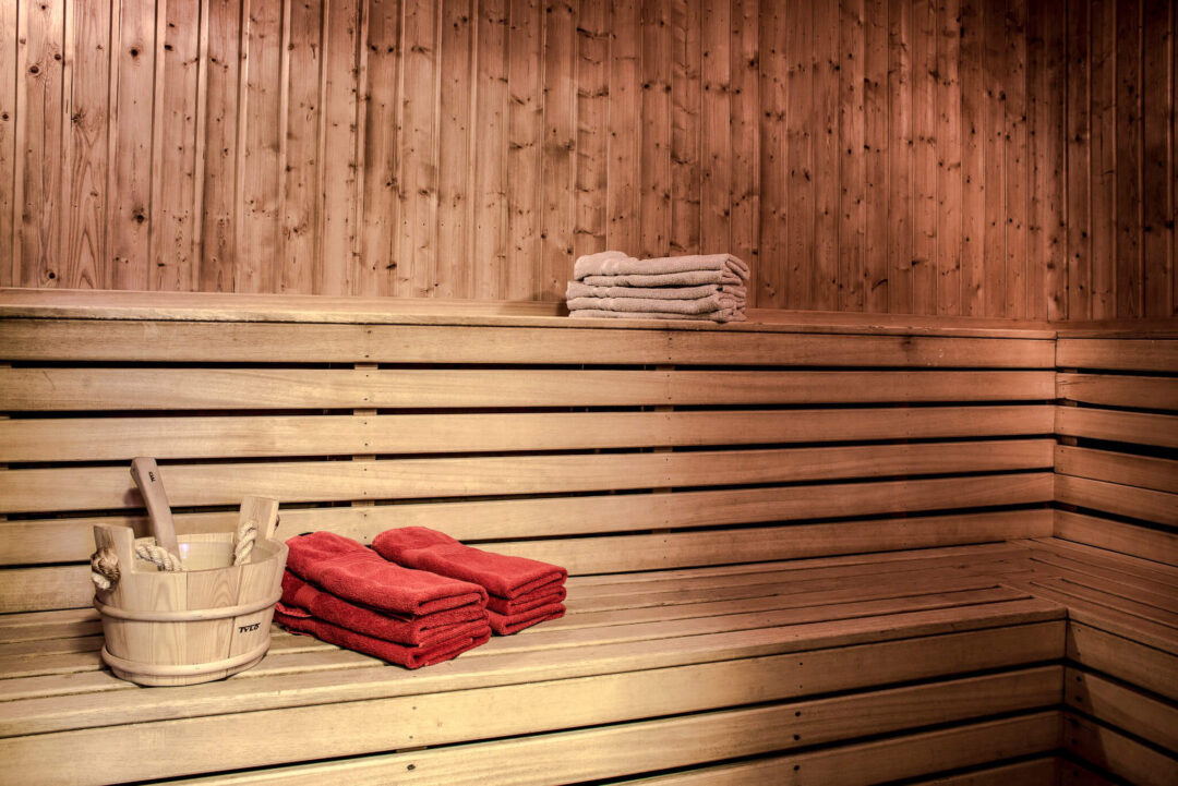 Wooden sauna interior with folded red towels and a sauna bucket for a warm spa break