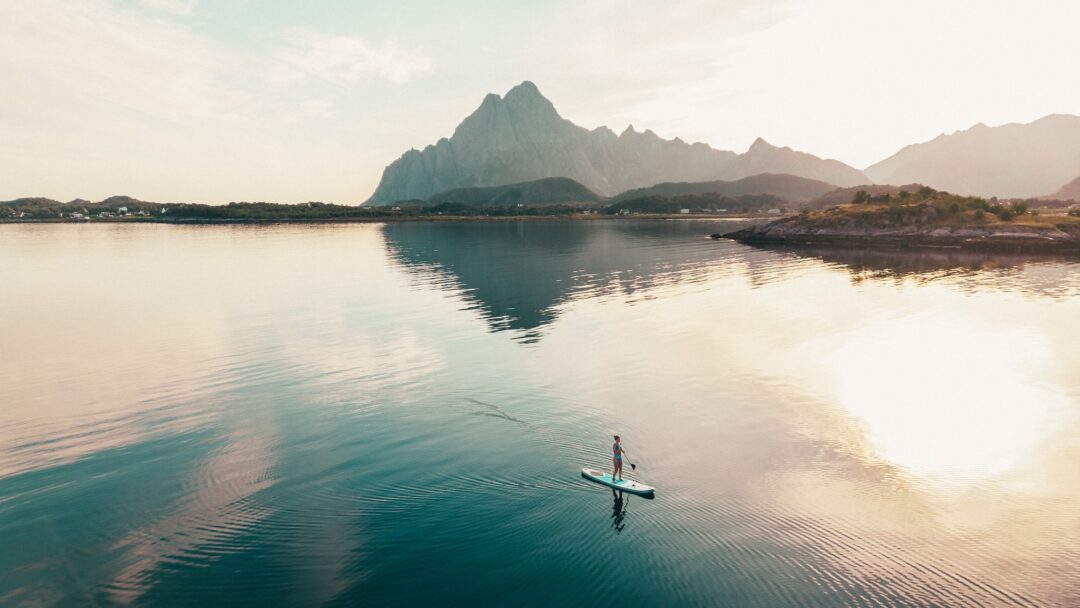Woman paddleboarding on a calm fjord near Lofoten mountains at sunrise