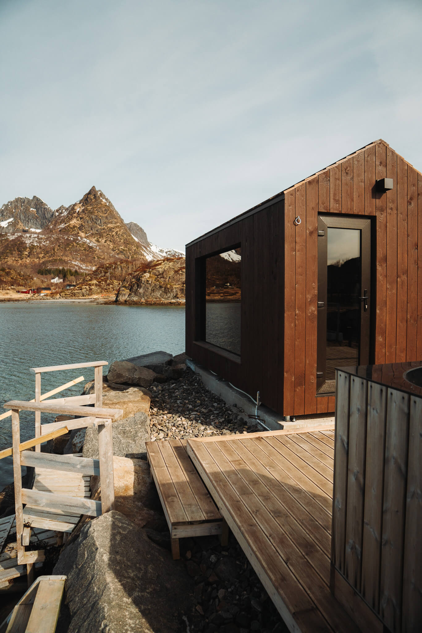Modern wooden cabin with deck by the fjord, snowy mountains in Lofoten, Norway