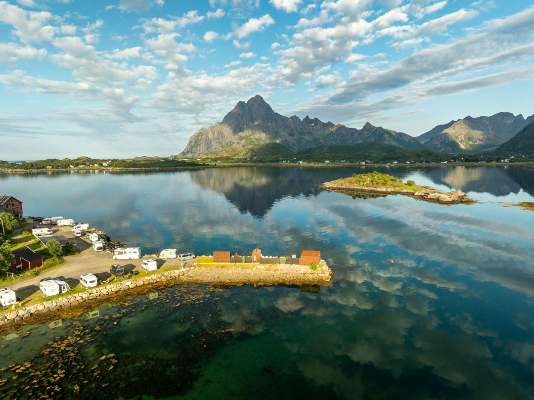 Aerial view of a calm fjord in Lofoten with houses, a small island and towering mountains