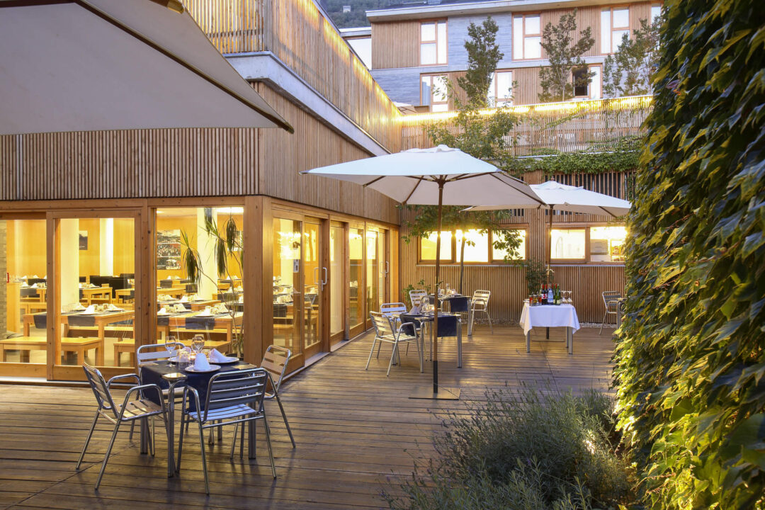 Outdoor café terrace with tables and umbrellas beside a building, suitable for a hiking holiday in the Spanish Pyrenees