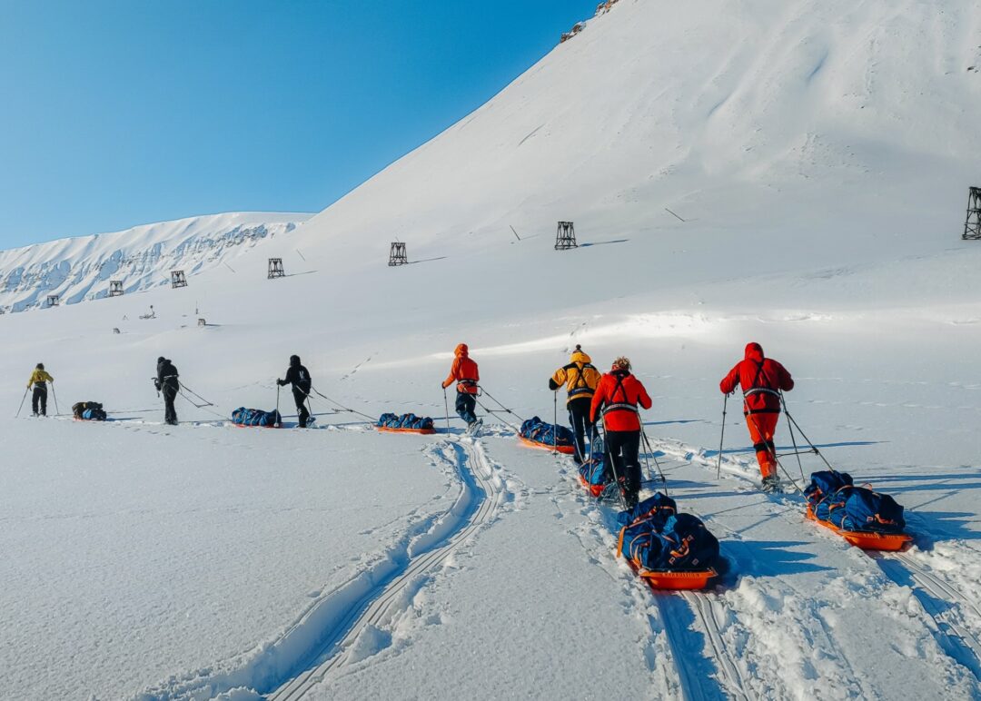 Snowshoeing group pulling sleds across snowy Svalbard mountains in Arctic winter