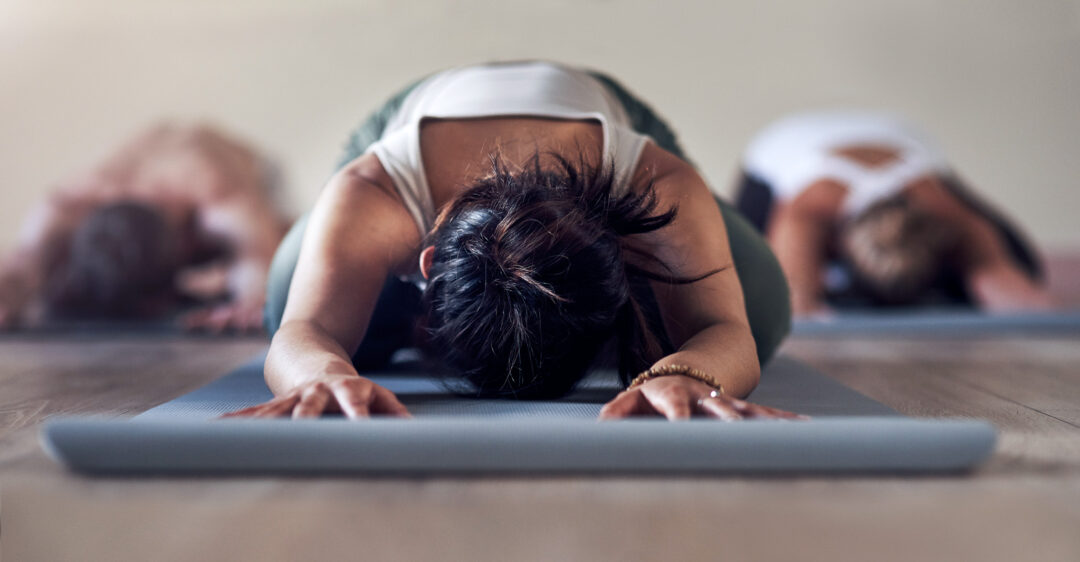 Yoga session: woman in child’s pose on a mat, with other participants stretching in the background