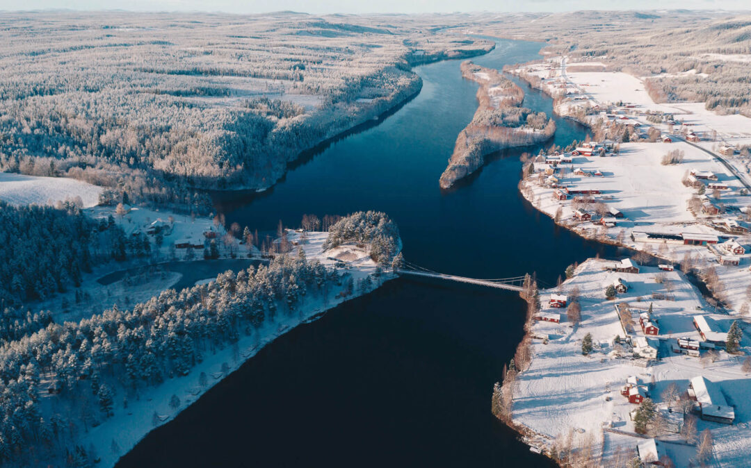Aerial view of a snowy Lapland river valley with winter cabins and forest banks in Lapland, Finland