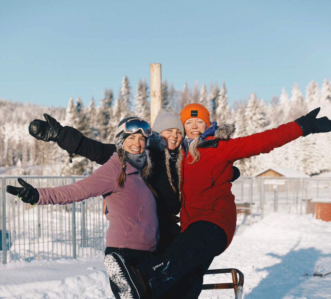 Smiling visitors in winter clothing ride a sled in Lapland snowy forest scenery
