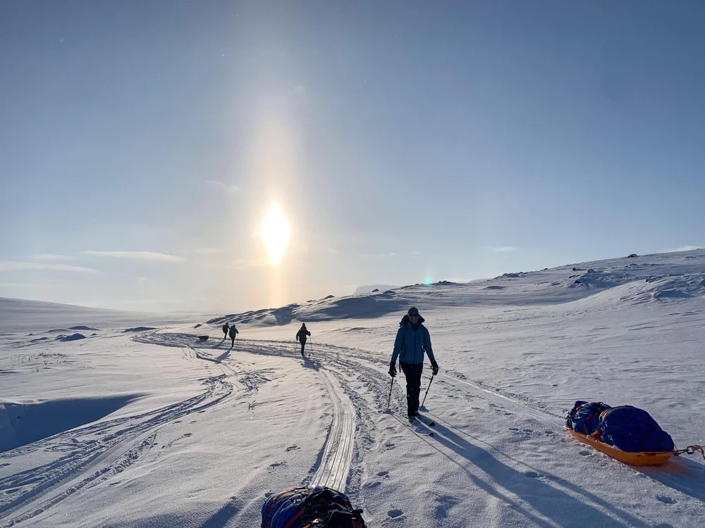 Women ski touring on a snow-covered ridge on a bright arctic-style trail under a clear sky