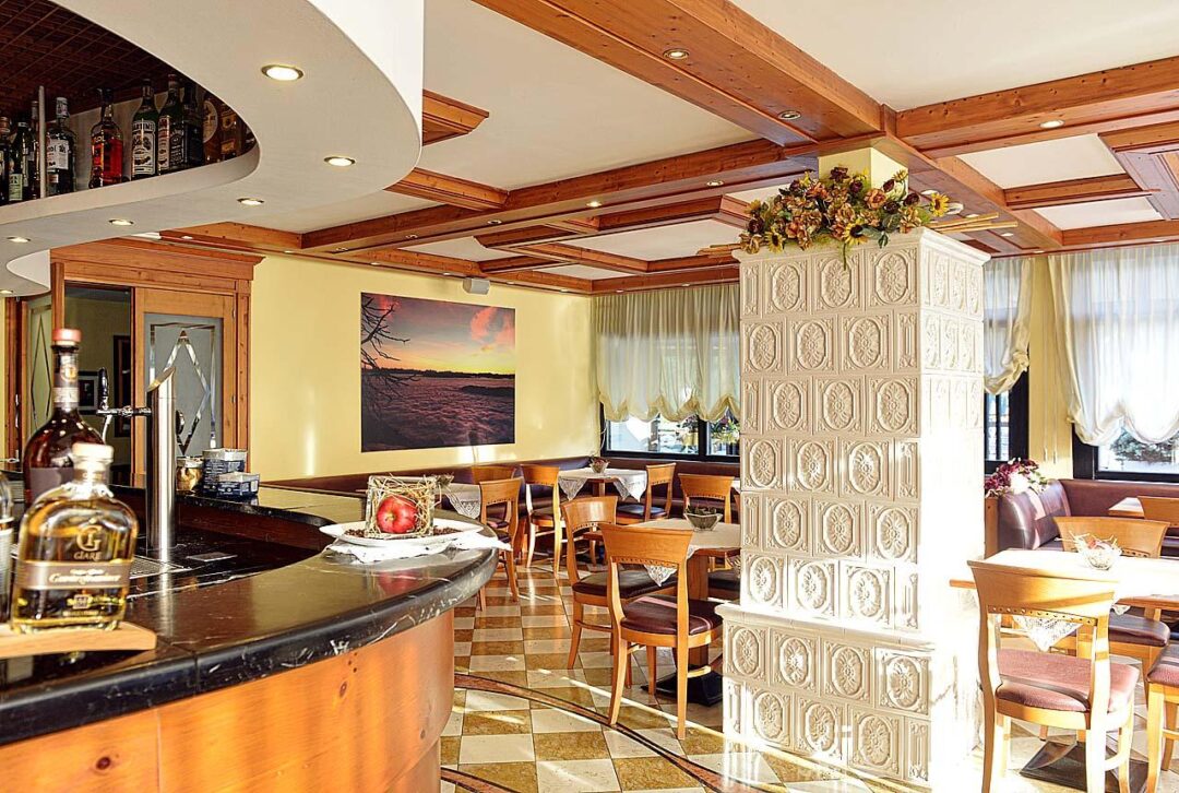 Dolomites hotel restaurant interior with bar counter, wooden beams and set tables for a guided snowshoeing stay