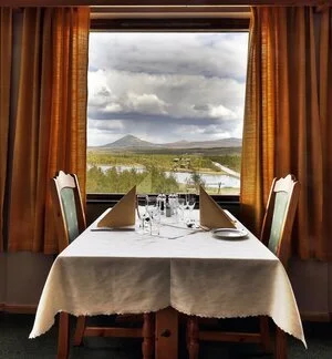 Cozy dining table by a large window overlooking snowy Norway mountains and a fjord, winter cross-country ski holiday view