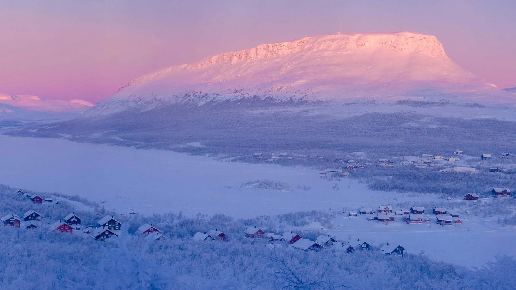 Snowy Arctic Circle village at dusk beneath a high mountain peak, ideal for a hut to hut ski expedition