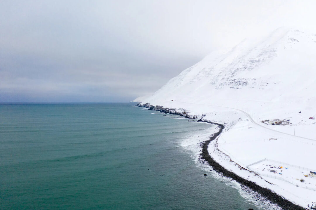 Snowy coastline along a fjord in North Iceland, with winter road and mountains under cloudy sky