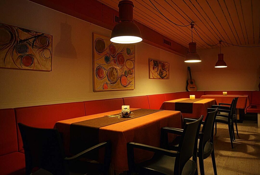Warm restaurant dining area with red booths, long table and pendant lights, inviting evening ambience