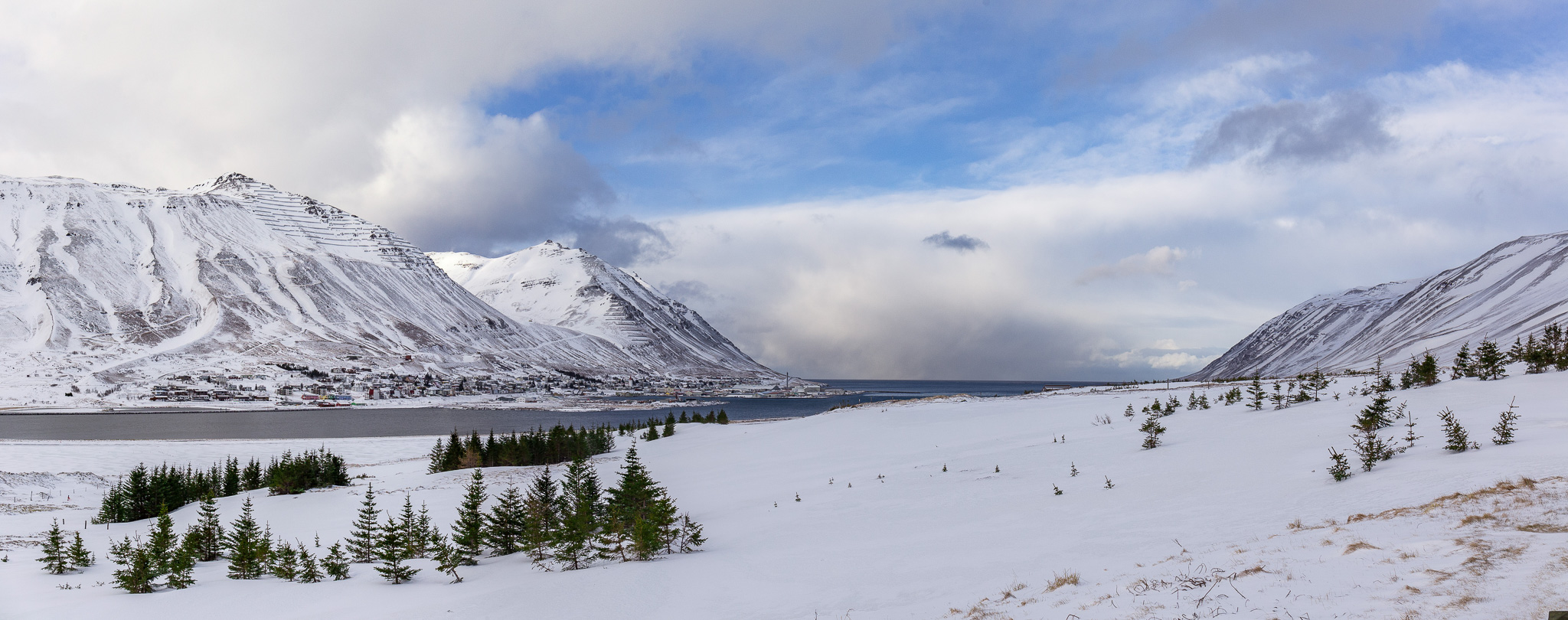 Snowy winter valley in North Iceland with fjord waters and mountains under cloudy skies