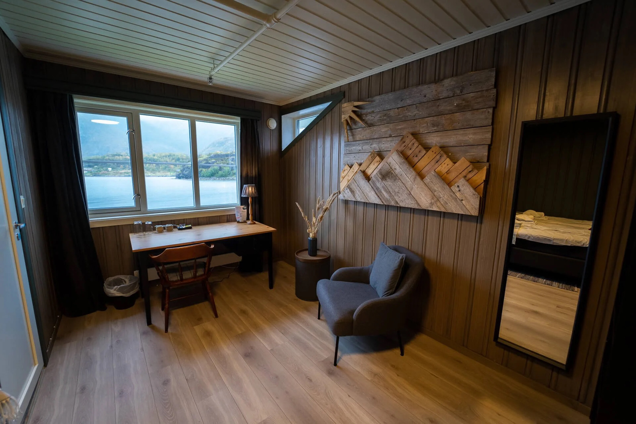 Coastal cabin interior with sofa and wooden walls, large window overlooking sea and mountains