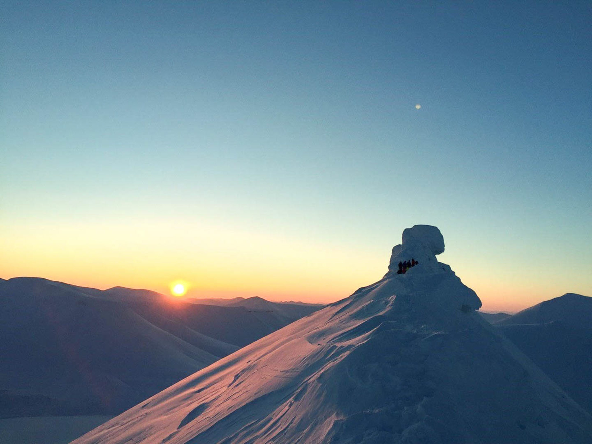 Woman snowshoeing at sunrise on snowy mountain ridge in Svalbard, Arctic landscape.