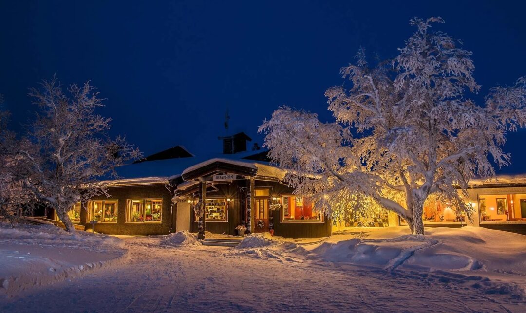 Snowy Norway winter lodge at night with warm-lit cabins and pine trees, perfect setting for a cross-country ski holiday