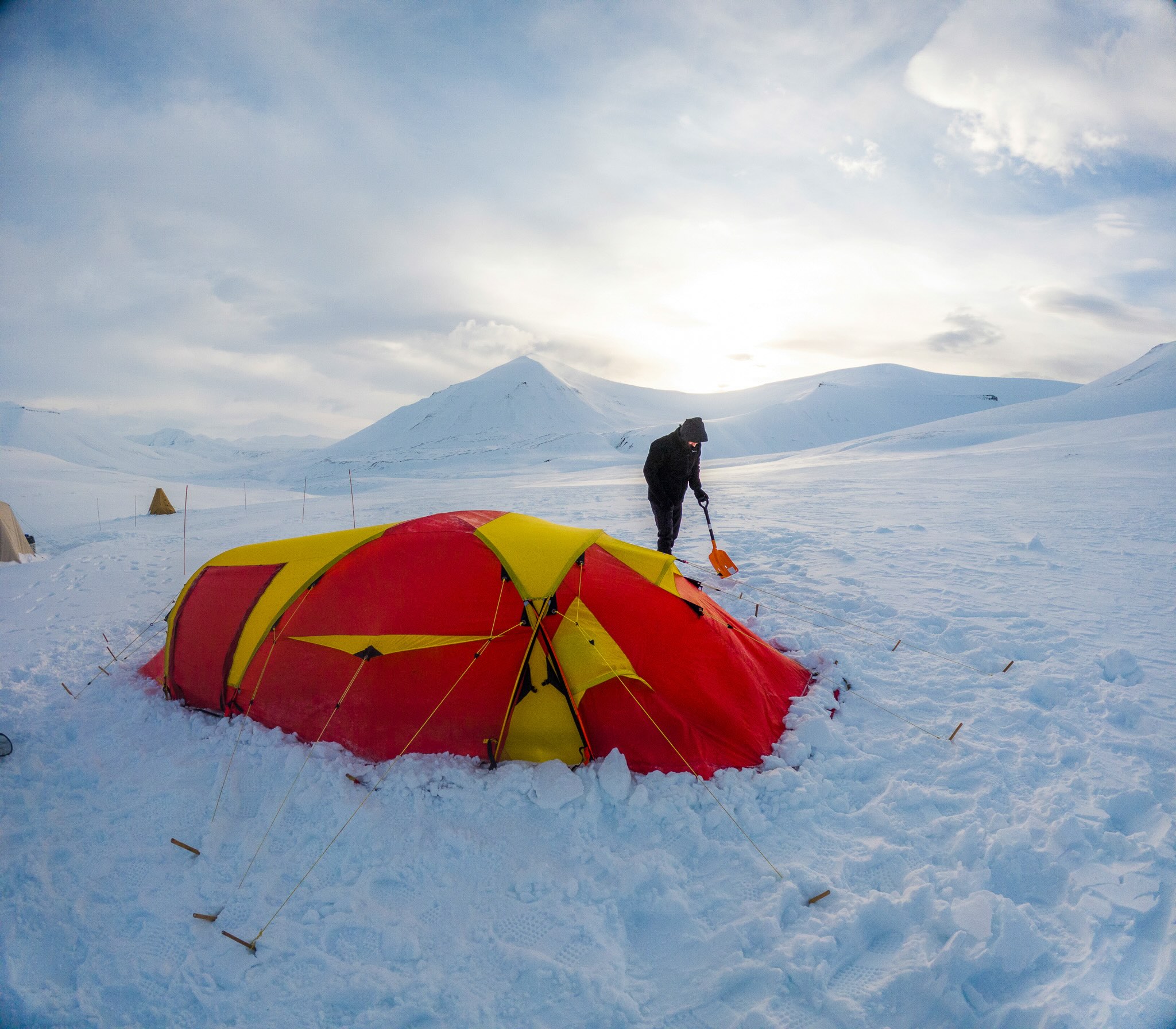 Woman beside a red tent on snowy Arctic ground in Svalbard, with mountains in the background.