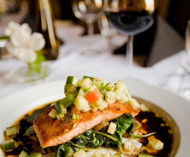 Salmon fillet topped with diced vegetables and herbs on a restaurant plate