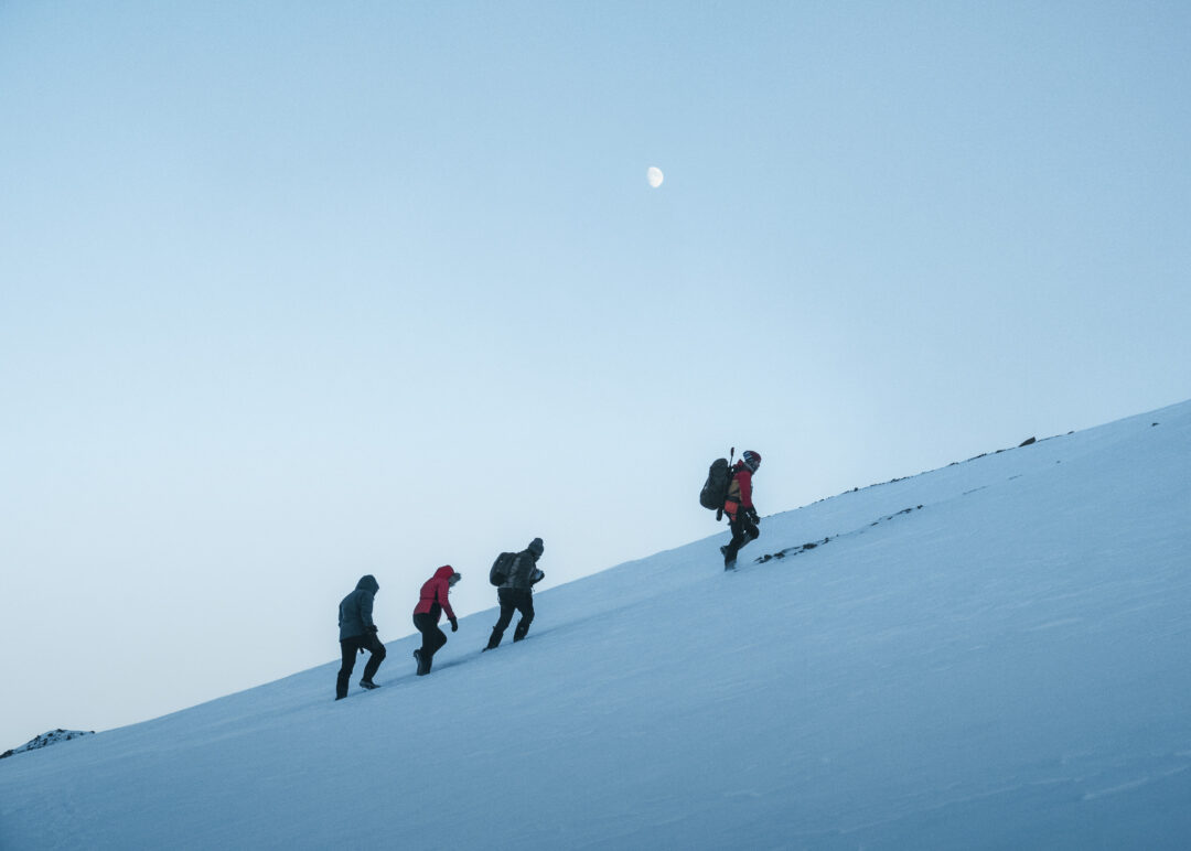 Women snowshoeing up a snowy Arctic slope in Svalbard during a wild camping expedition