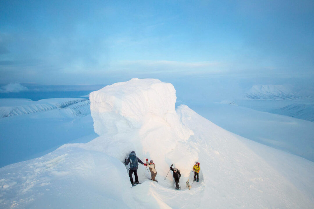 Snowshoe hikers trek across snowy Arctic terrain on a ridge under a clear blue sky