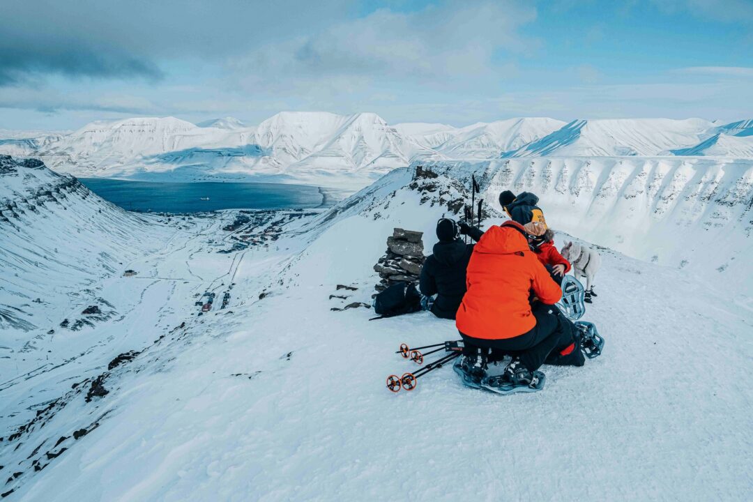 Women with snowshoes and backpacks on a snowy ridge, overlooking Svalbard mountains.