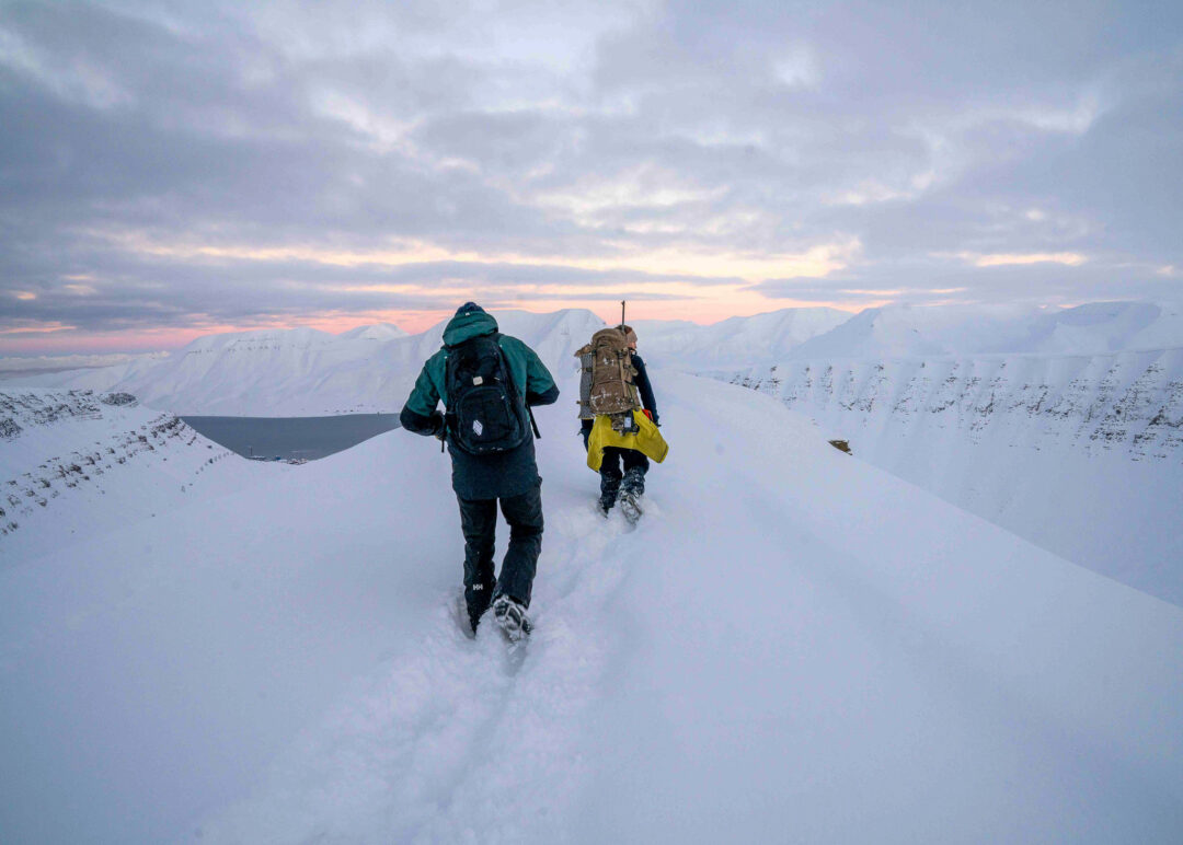 Women snowshoeing on snowy ridgeline in Svalbard Arctic at dusk, with backpacks for wild camping expedition
